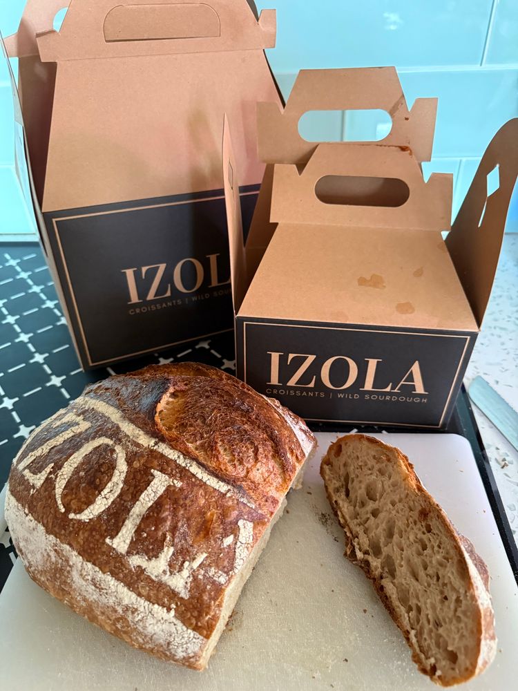 Two boxes with Izola logo on it and a loaf of wild sourdough bread with one slice cut out of it. 
