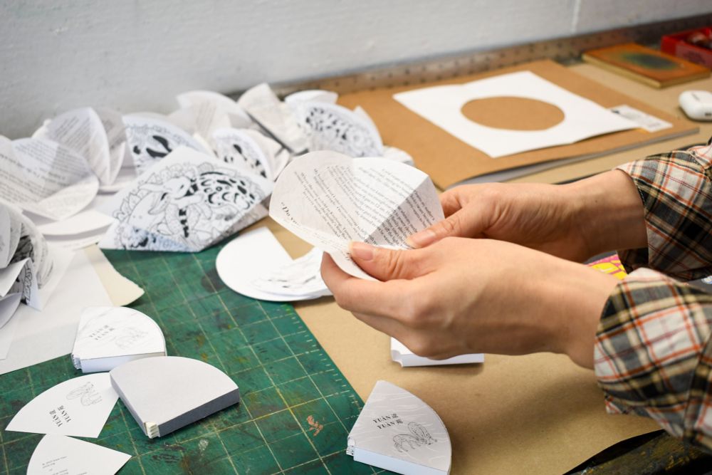 Close-up of Jenie’s hands folding prototypes of a new artists’ book shaped like a circle.