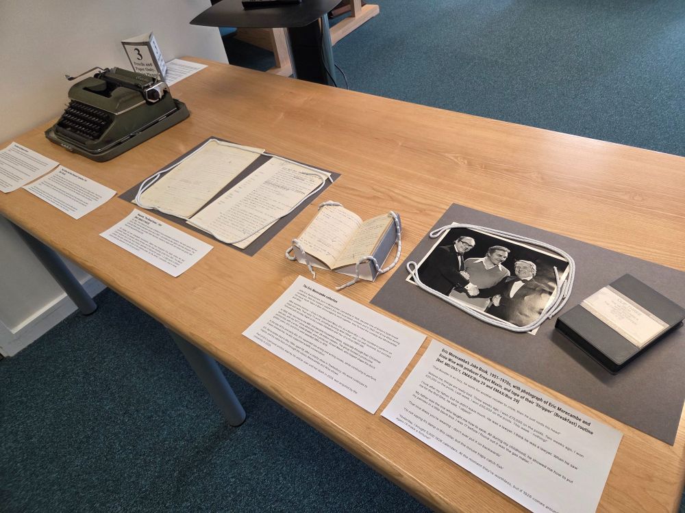 A table with an old fashioned typewriter on the left hand side, with a number of historic documents laid out across the rest of the table. There is also one black and white photograph. 