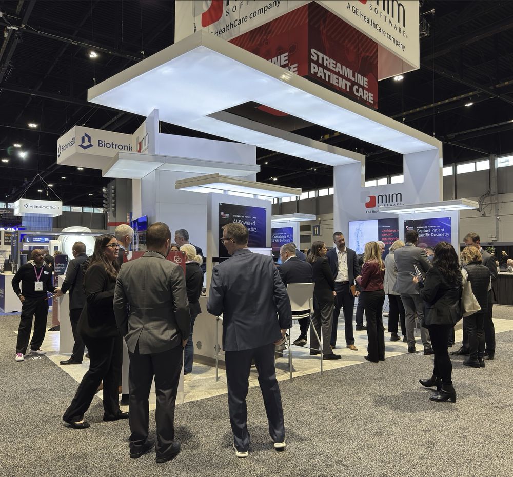 People standing in and around the MIM Software booth at RSNA 2024. Booth signs are visible that read "MIM Software, a GE HealthCare company" and "Streamline Patient Care."