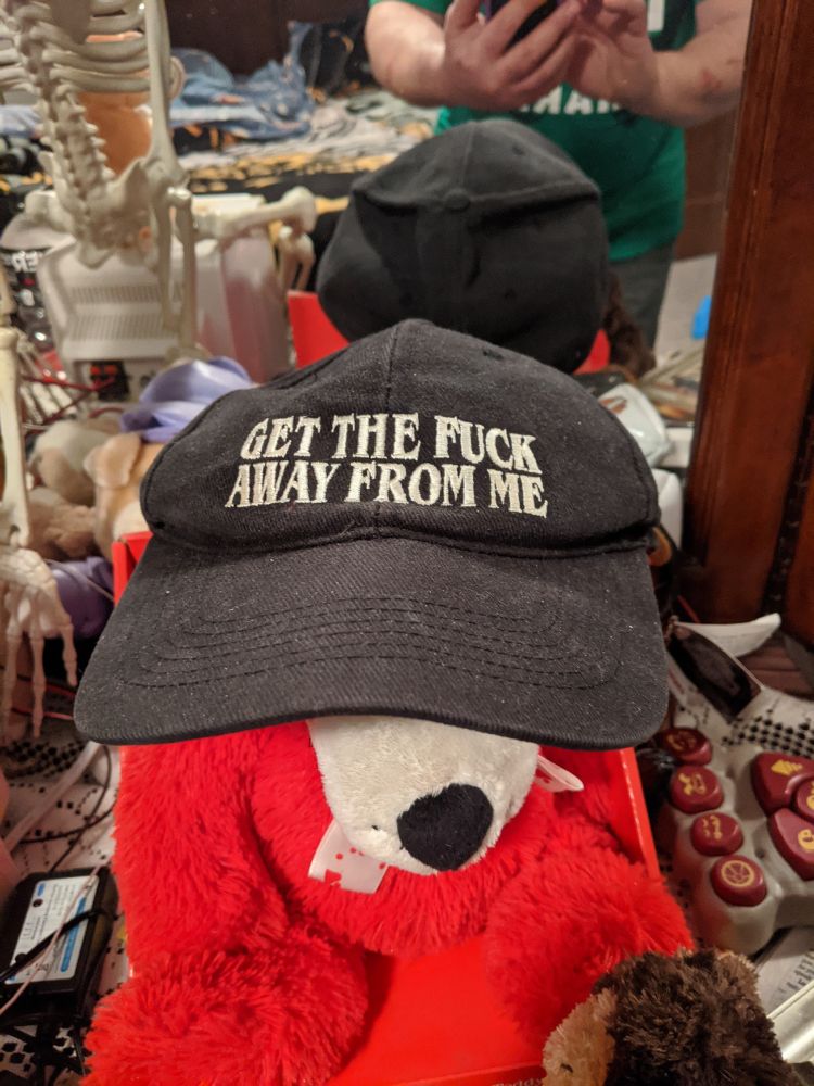A black baseball cap with the words "GET THE FUCK AWAY FROM ME" embroidered in white thread