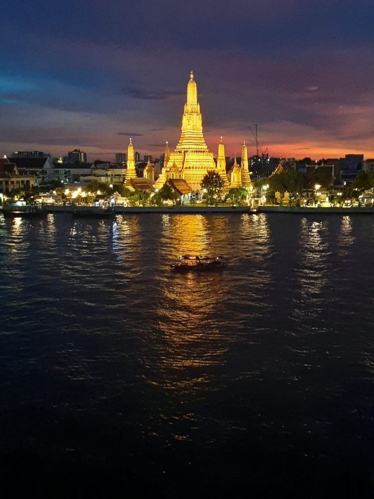 Imagen que muestra un templo budista iluminado frente al río Chao Praya en Bangkok.