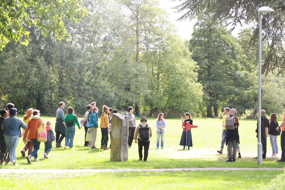 a group of people in a green space with trees in the background, gathering around a woman holding a large red key