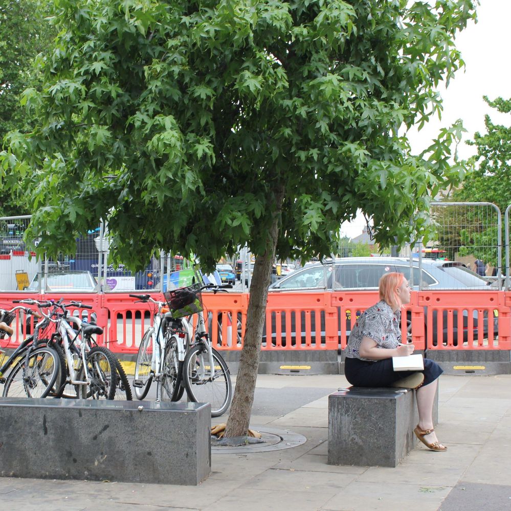 A woman with pink hair sitting on a bench, observing her surroundings