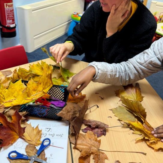 an aduklt and child doing crafts with autumn leaves