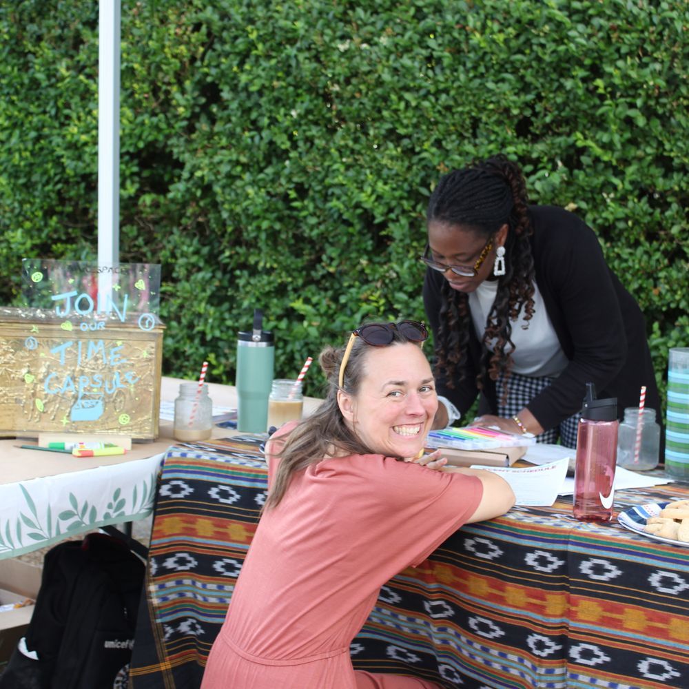 A woman in the foreground leaning on a table, smiling for the camera