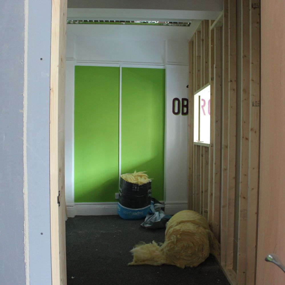A room with a partially finished stud wall and a roll of insulation on the floor