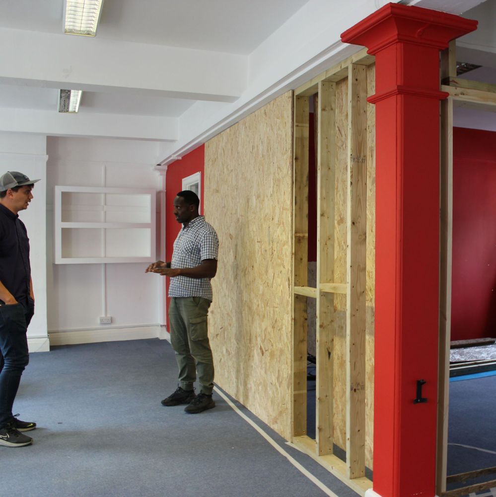 two people in conversation in a room with a partially completed OSB wall