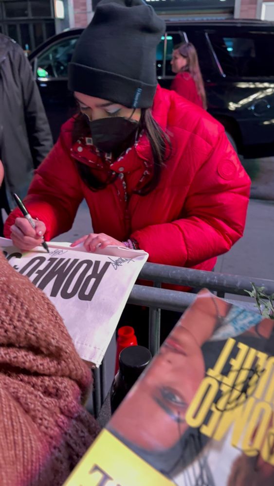 rachel zegler in a red puffer jacket, black beanie, and mask signing my romeo and juliet bag at stage door in new york city 
