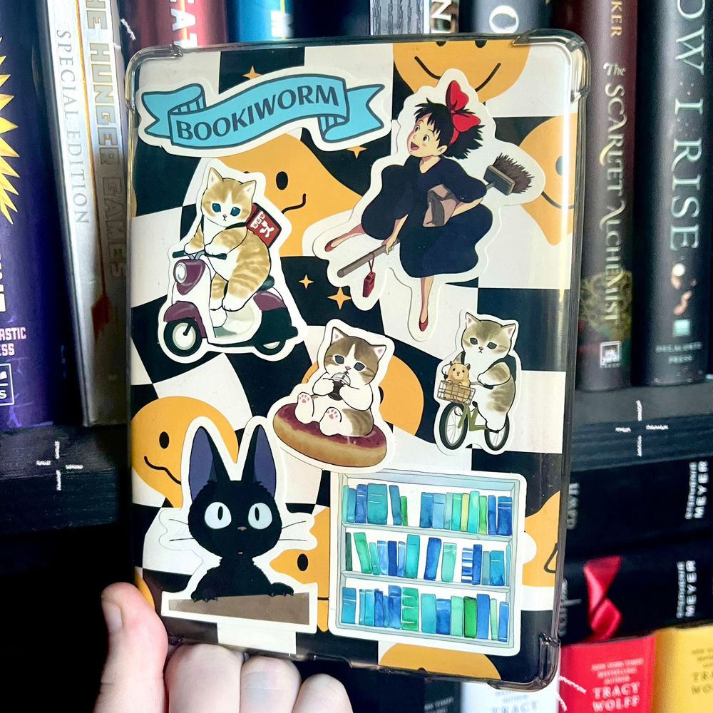 Black & white checkered background with yellow smiley faces

Stickers: “bookworm” on a banner, Kiki on a broom from Kiki’s delivery service, a cat on a moped, a cat sitting on a doughnut sipping a coffee, a cat riding a bike with a hamster in the front basket, jiji from Kiki’s delivery service & a square of bookshelves showing various shades of blue spines