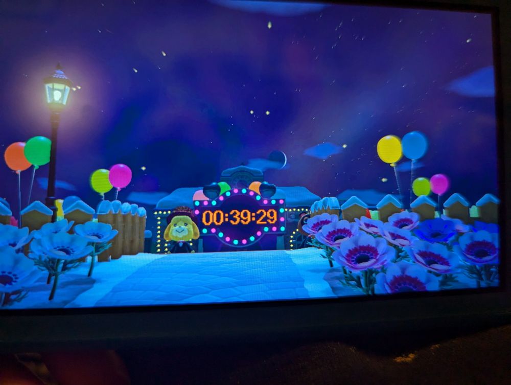 A screenshot from Animal Crossing New Horizons. The New Years Display is lit up with 39 minutes to go. In the background you can see a pink aurora. 