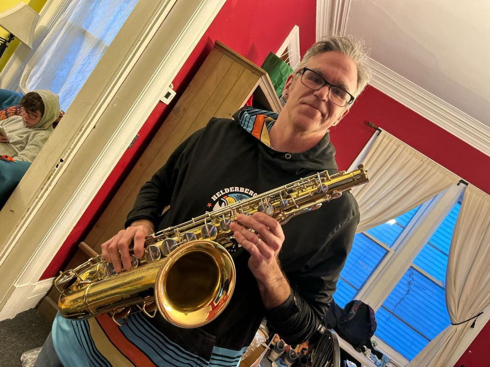 Photograph of a dorky man holding a tenor saxophone and smiling a dorky smile.