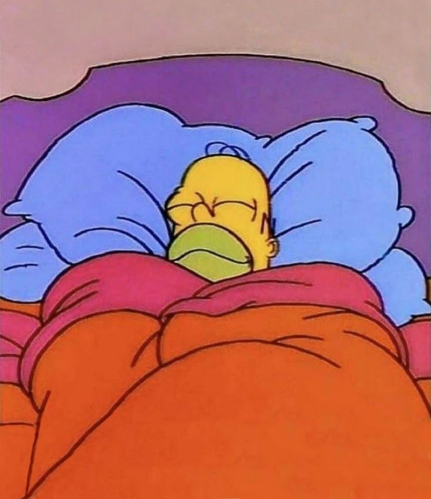 Homer Simpson liegt eingekuschelt und mit zufriedenem Gesichtsausdruck im Bett