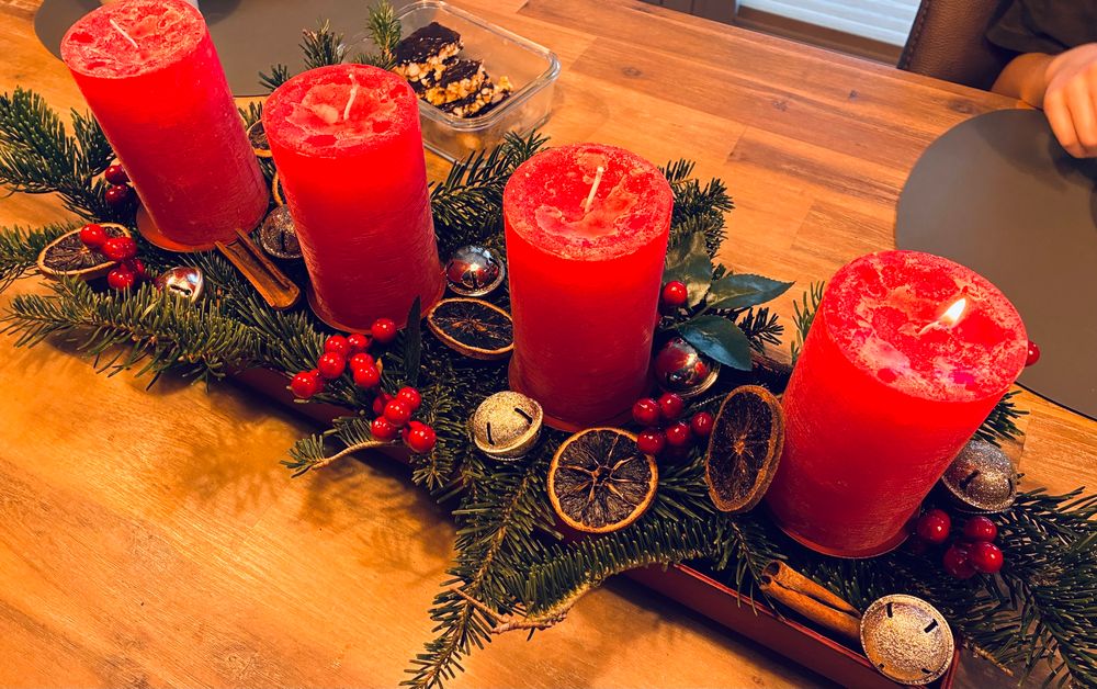 Adventskranz mit roten Kerzen auf einem Esstisch. Die erste Kerze brennt. 