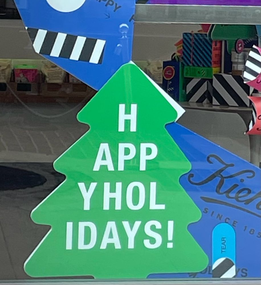 A Christmas tree sign with letters going from top to bottom spelling out “HAPPY HOLIDAYS!”.