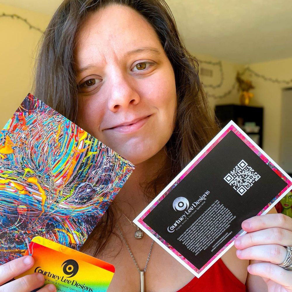 A photo of Courtney Lee Designs (September 2025) holding her business card, and two colorful postcards. Full caption below:

“So far, I’ve distributed small samples of these colorful postcards at:

• Record Archive
• The House of Guitars
• Seymour Library
• Lift Bridge Book Shop
• GamePlayers Brockport
• Hart Gallery 27

Where will these beauties end up next? 🤔💭🌈❤️

courtneyleedesigns.com
patreon.com/courtneyleedesigns”