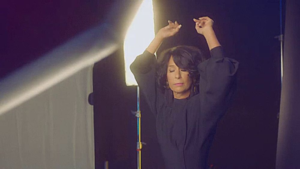 a woman in a black dress is standing in front of a light with her hands in the air