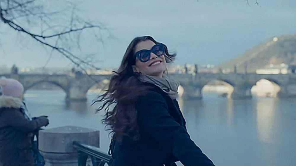 a woman wearing sunglasses is smiling in front of a bridge