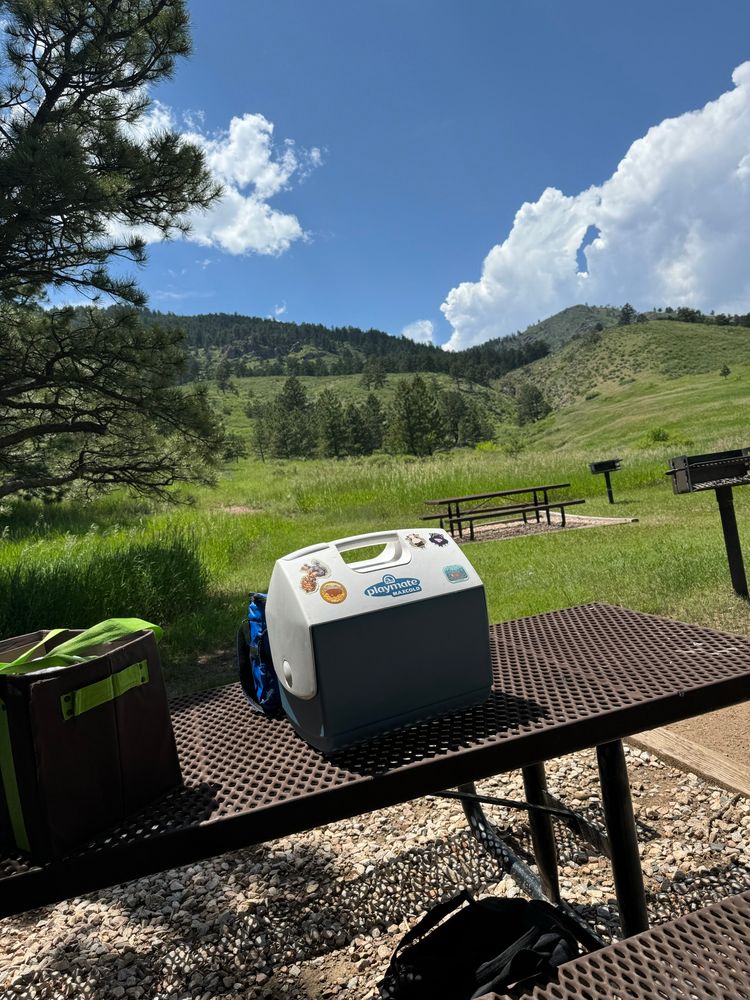A photo of a cooler at a picnic area in front of grassy hills. 