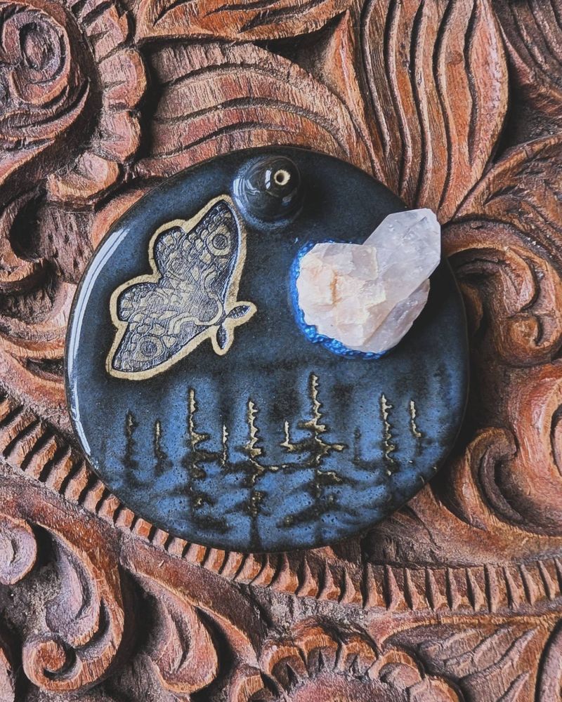A deep blue ceramic incense burner adorned with a forest scene, a stamped moth, and a raw quartz.