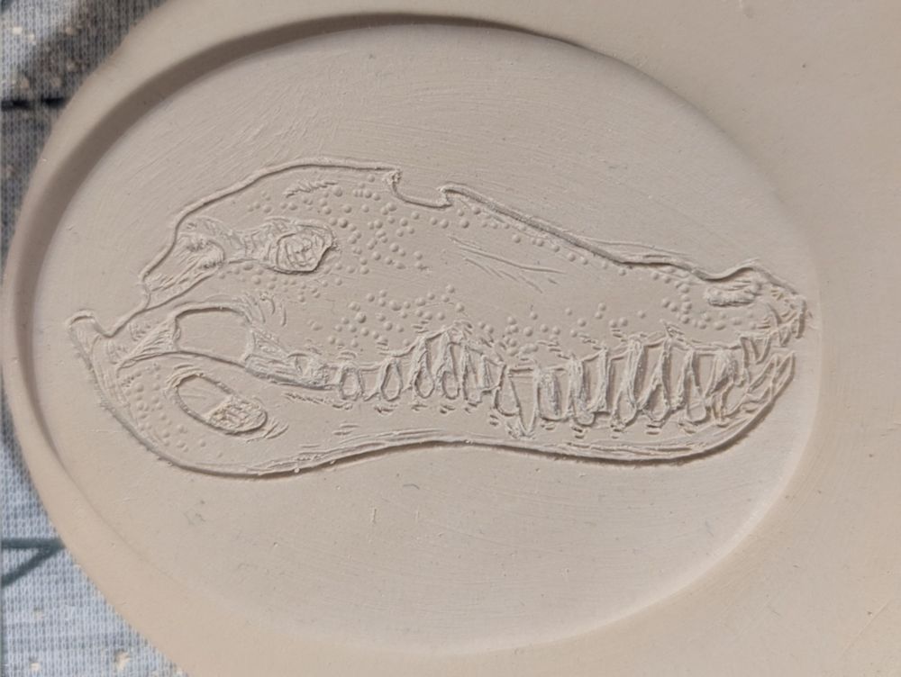 Close up photo of the drawn image of an alligator skull drawn on a clay emblem.