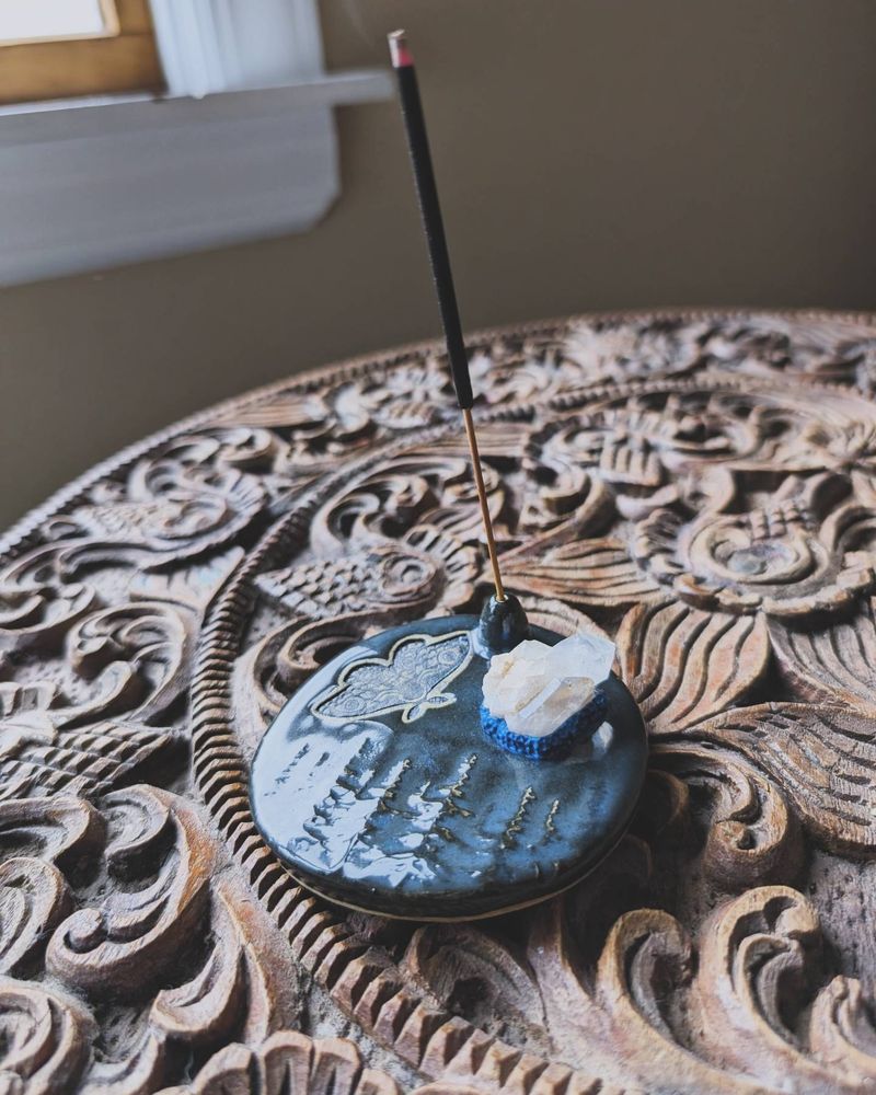 The same incense holder at an angle with a black incense stick burning. 