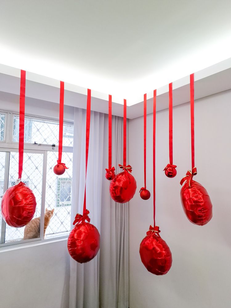 Foto de uma parede branca intercedendo por uma parede com cortinas brancas. No teto de e balões vermelhos redondos pendurados por fitas vermelhas