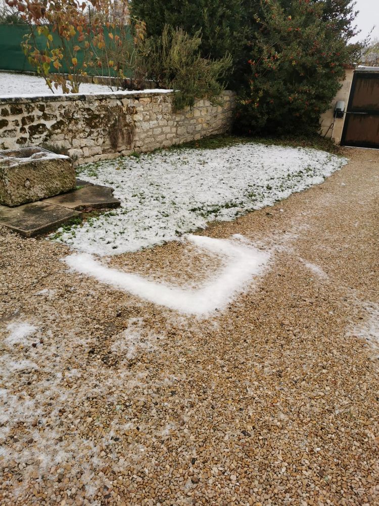 Photo d'une cour un peu enneigée. La neige a globalement fondu, il en reste un peu sur un carré d'herbe. Dans la cour en gravillon, la neige n'a pas fondu à un endroit, formant un carré de neige.