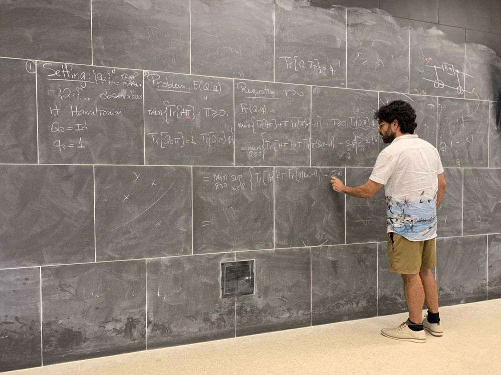 Augusto Gerolin writing optimal transport equations on the QuNB floor to ceiling blackboard 