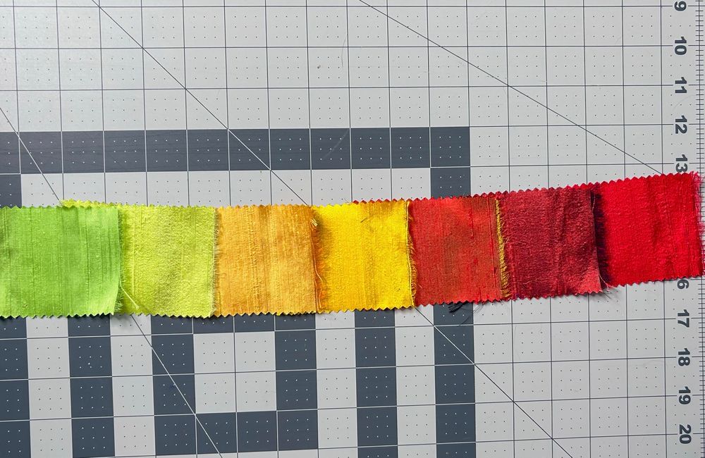swatches of silk ranging from light green, yellow, orange, to red, lying on a grey cutting mat