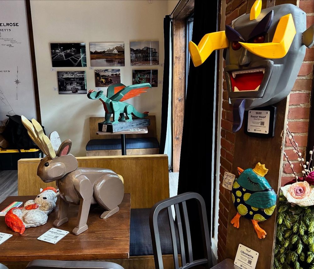 A clay unicorn, a wooden jackalope, a wooden dragon, the face of a wooden djinn, and a clay bird on display in a brewery 