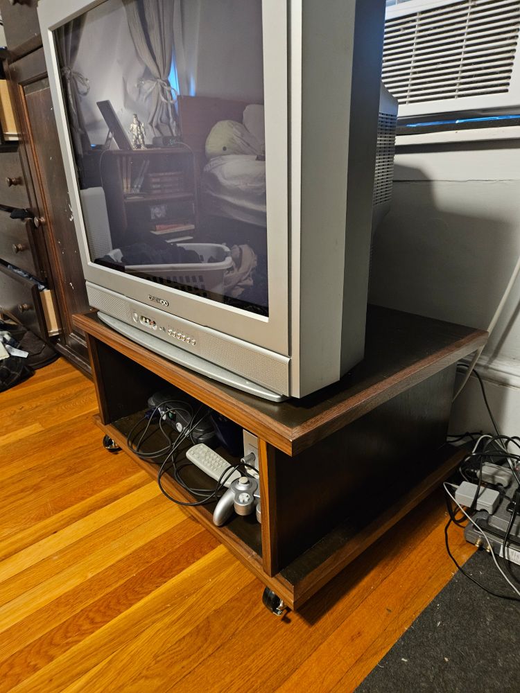 A short walnut and plywood TV stand on casters. There is a game cube and a Nintendo 64 inside the open cabinet