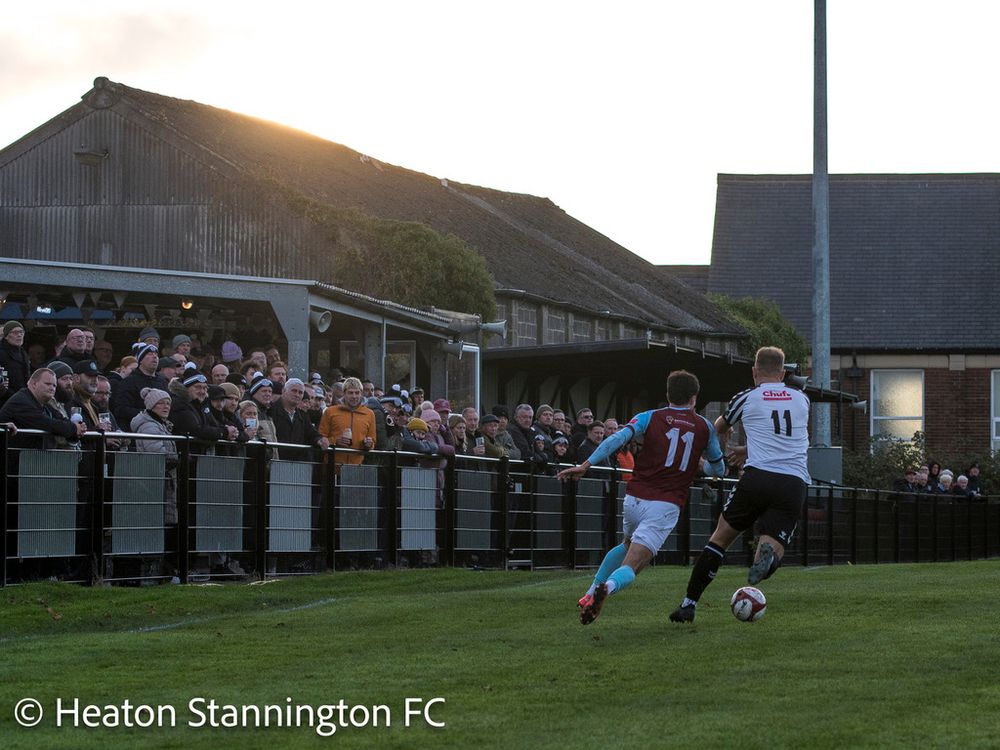 Two footballers running away from the camera, watched by a large crowd. 