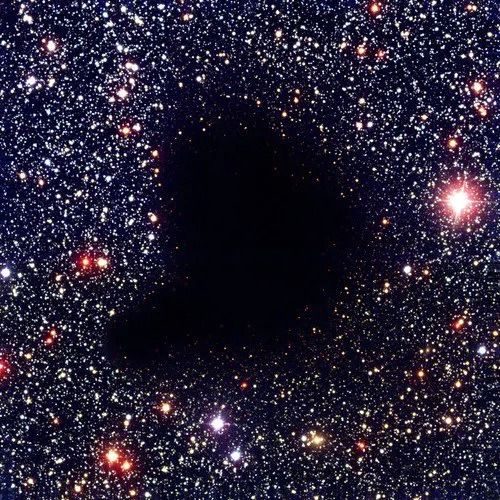 a imagem de fundo preto mostra milhares de estrelas amarelas, vermelhas, azuis e principalmente brancas, algumas um pouco maiores que outras. na parte central da imagem, vemos uma região em formato irregular completamente preta