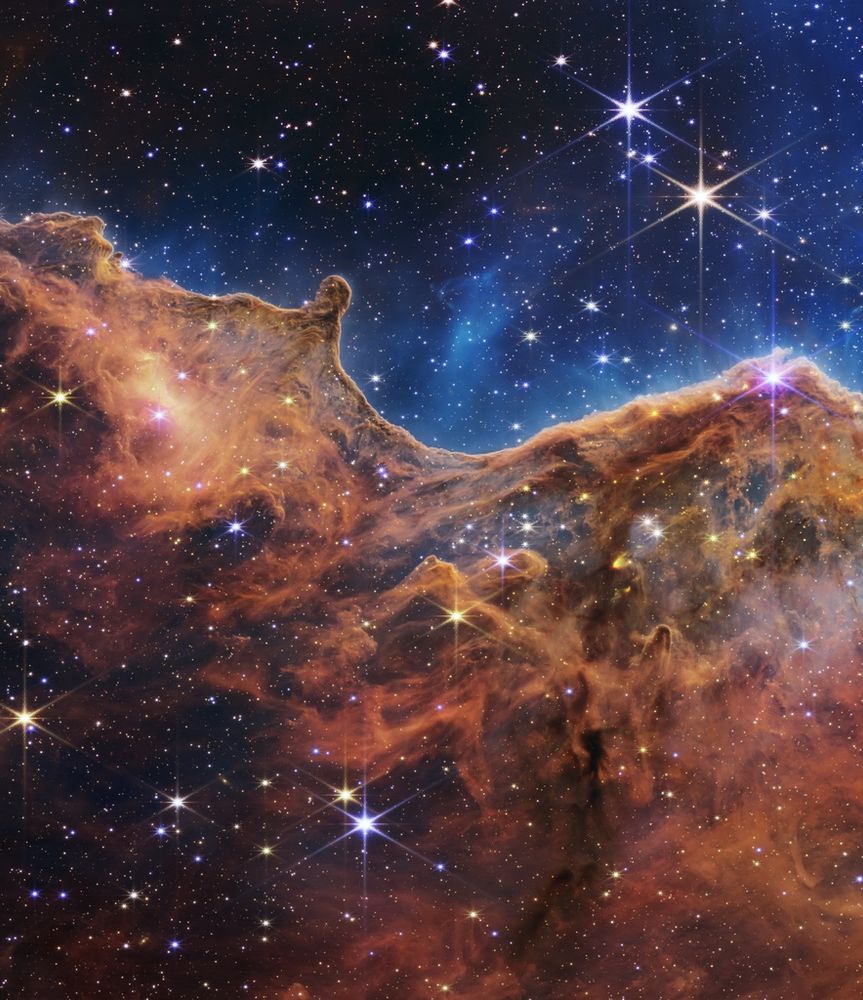 a imagem mostra uma grande nuvem amarronzada, bastante opaca, que cobre toda a parte inferior da imagem até um pouco acima da metade. essa nuvem tem algumas partes mais escuras, e algumas estrelas pontuais brilhantes podem ser vistas dentro dela. acima dessa estrutura, vemos o resto da imagem azulada, também com algumas estrelas ao fundo