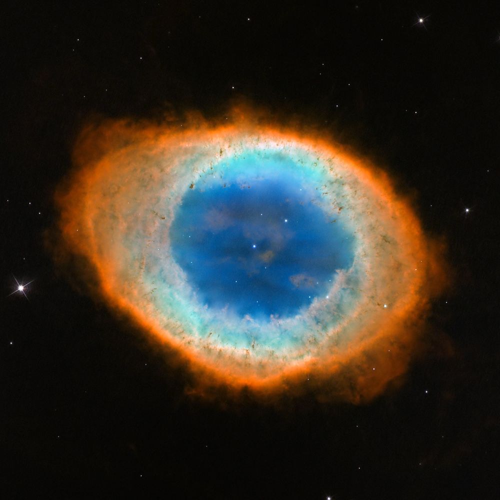 a imagem mostra uma estrutura circular, semi opaca, que tem um tom azul escuro na parte central, e conforme vai mais para fora vai ficando mais azul claro e, por fim, alaranjado. também vê-se uma estrela brilhante bem no centro da estrutura