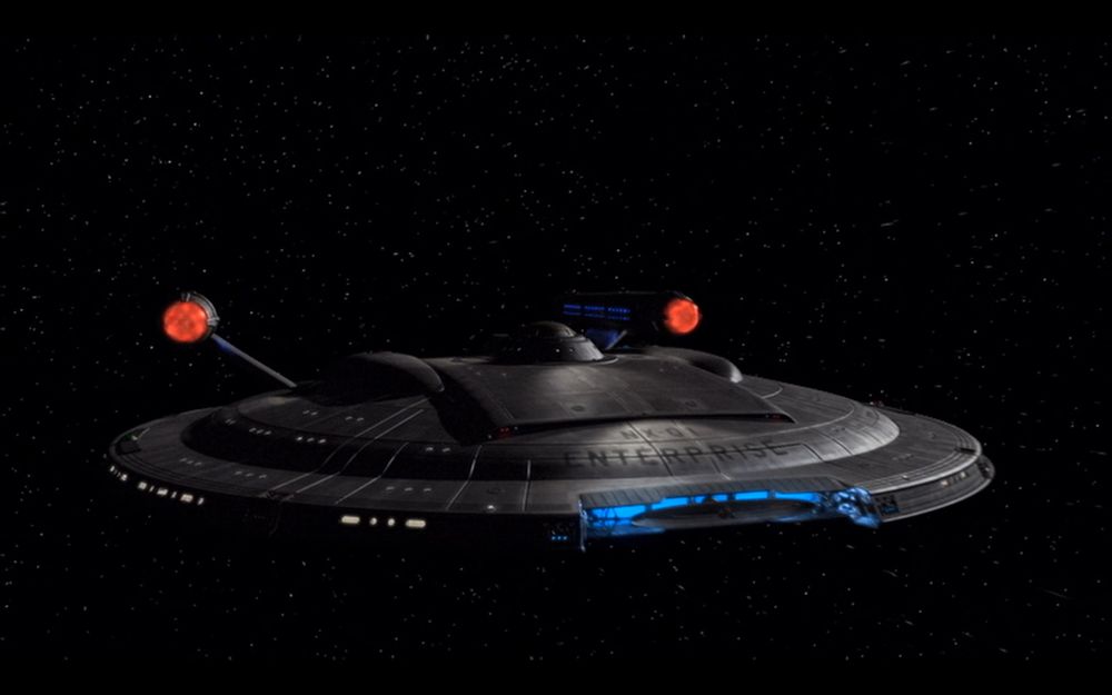 The Enterprise NX-01 seen from the front, slightly to the side. She's flying on a dark sky, with only a handful of stars visible.