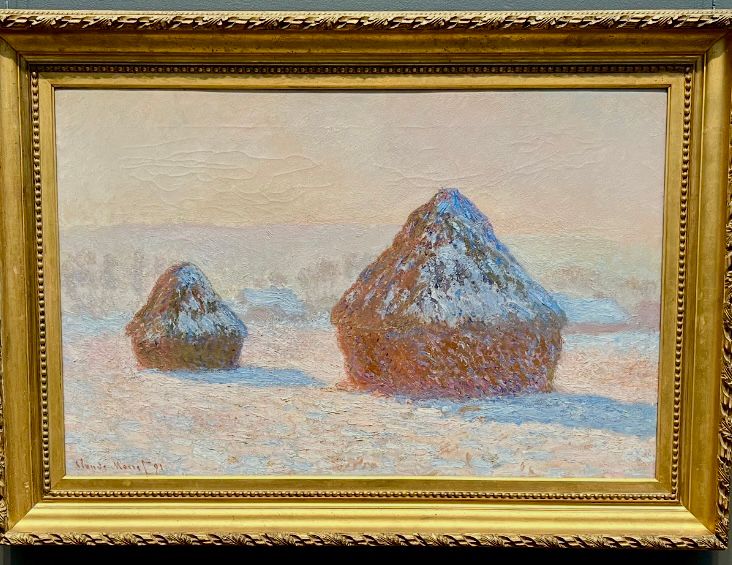 Two stacks of wheat, snow on the ground, subtle snow effects on mostly one side of the wheat stacks. Bright, sunlight glimmering. Impressionist style painting. 