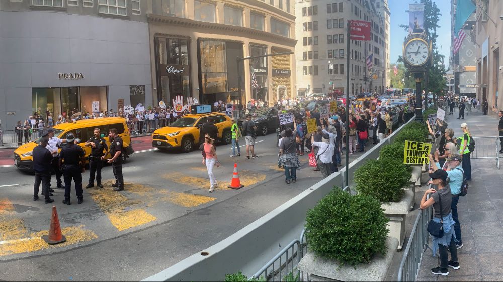 Crowds of protestors line both sides of Fifth Avenue holding signs including "No Troops In Our Cities." Police stand around as taxis pass down the streets.