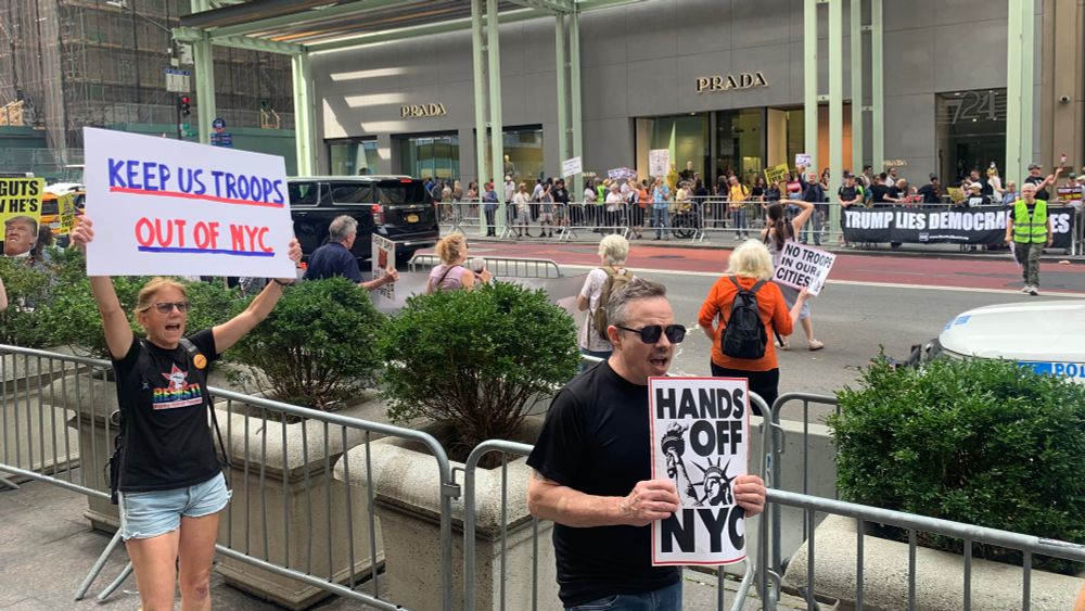 Protestors outside of Trump Tower hold up signs saying "Keep US Troops Out of NYC" and "Hands Off NYC."