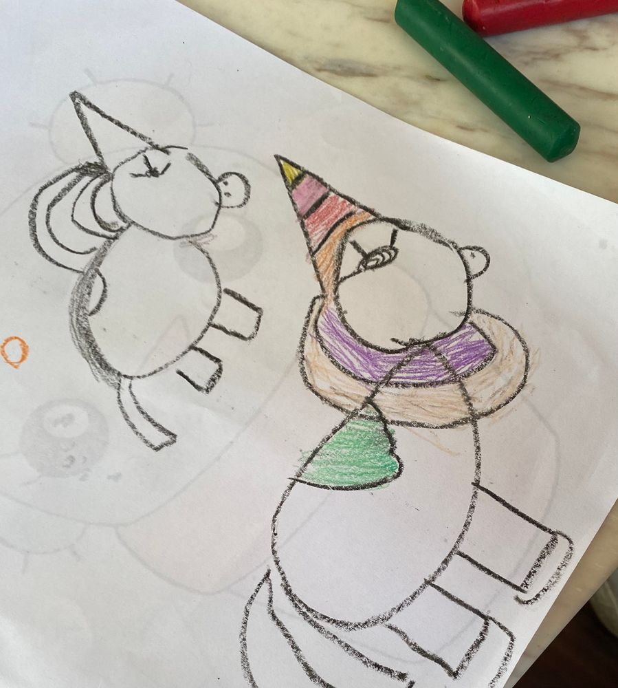 Two unicorns drawn by a 4-year-old child using crayons. One is in black and white; the other one has a colorful horn and something that looks like a necklace around its neck. 