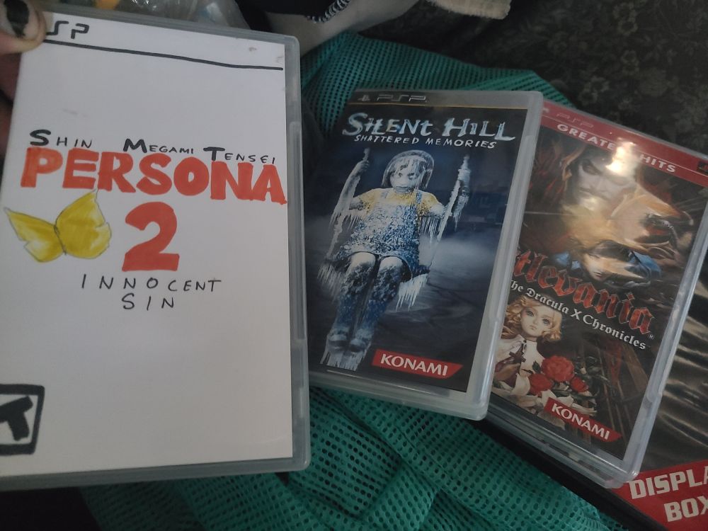 Several games for Sony Playstation Portable (PSP) are haphazardly laid out. From left to right: Shin Megami Tensei Persona 2 Innocent Sin, Silent Hill Shattered Memories, and Casylevania Dracula X Chronicles.