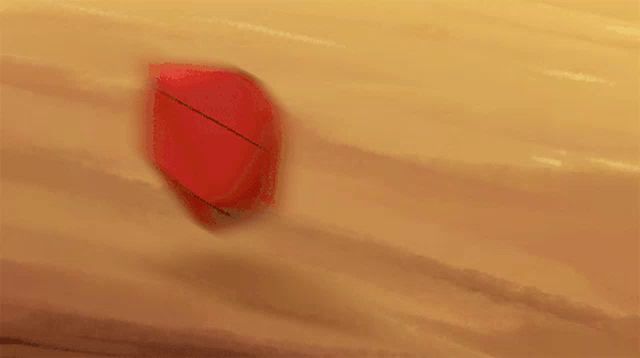 a red cube is sitting on top of a sandy surface