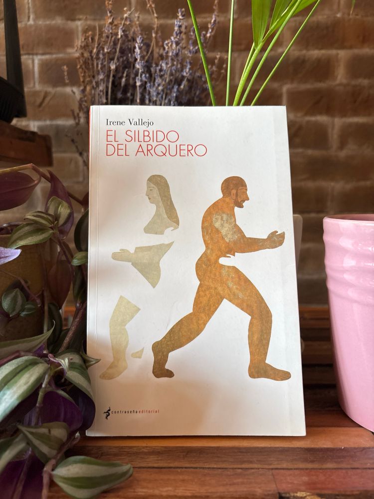 Fotografía de la portada del libro #elsilbidodelarquero con un fondo de plantas. La portada refleja a un hombre musculoso y a una mujer que se han cruzado y caminan ya caminos opuestos. Figuras de pinturas clásicas.