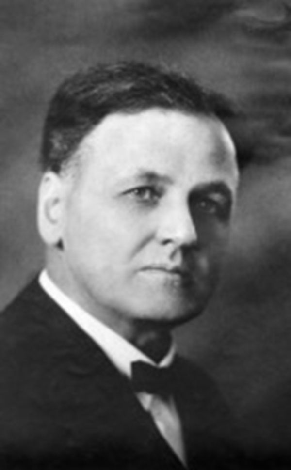 Black and white photo of a white man. He has a high forehead and is wearing a dark suit and what is perhaps a small bow tie.