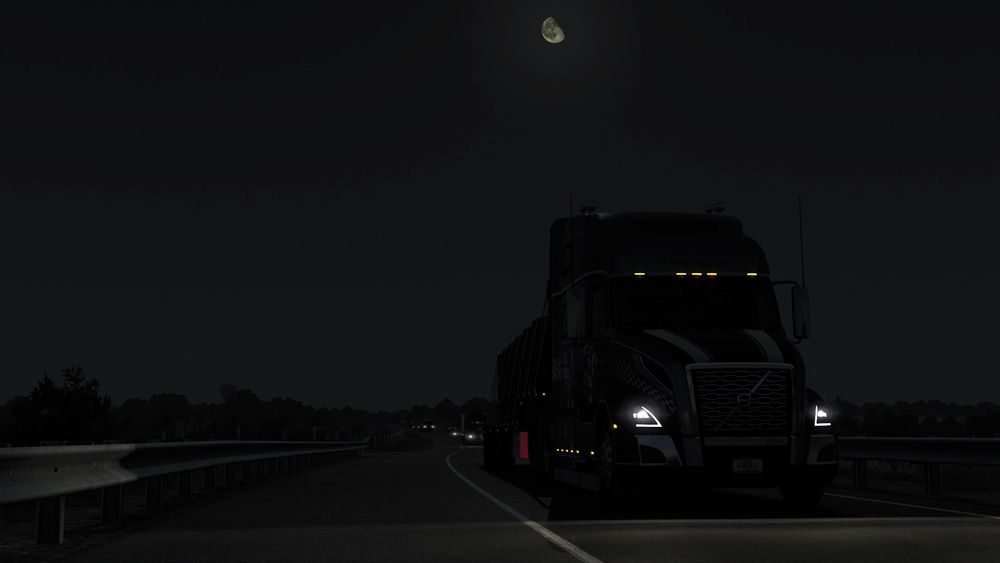 The Volvo VNL seen from the front, looking up at the truck on a single-lane road. It’s the middle of the night, illuminated only by a three-quarter moon. Several vehicles are following behind.