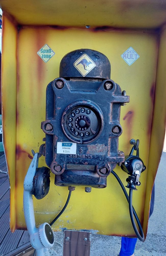 Ein sehr alter SIEMENS Fernsprechapparat in Schwarz, hängend
Mit Wählscheibe, Hörer der links an einem Haken hängt 
Rechts ein Kabel mit einer Buchse, die ebenfalls auf einen Haken gehängt wurde