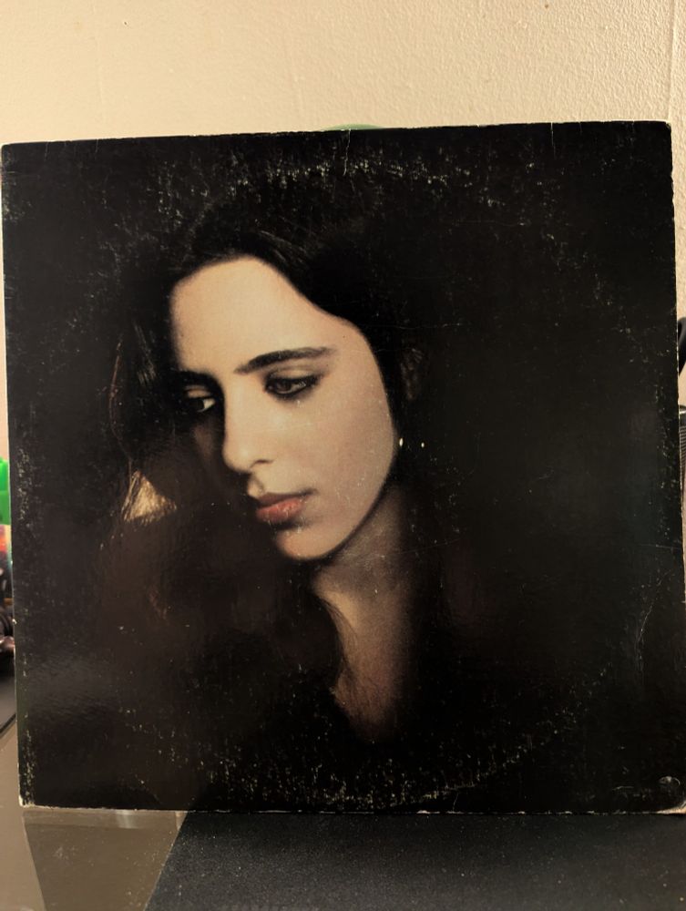 Record album cover of headshot of a young white woman with dark hair looking away. She is dressed in black against a black background.