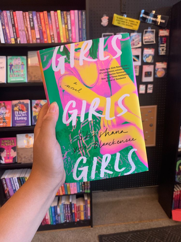 Casey holds up a copy of Girls Girls Girls by Shoshana von Blanckensee. 