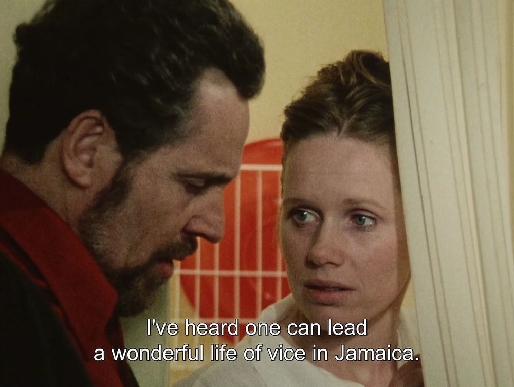 a frame from the film FACE TO FACE. a man looks downwards while a woman looks at him. the subtitles read: "I've heard one can lead a wonderful life of vice in Jamaica." 